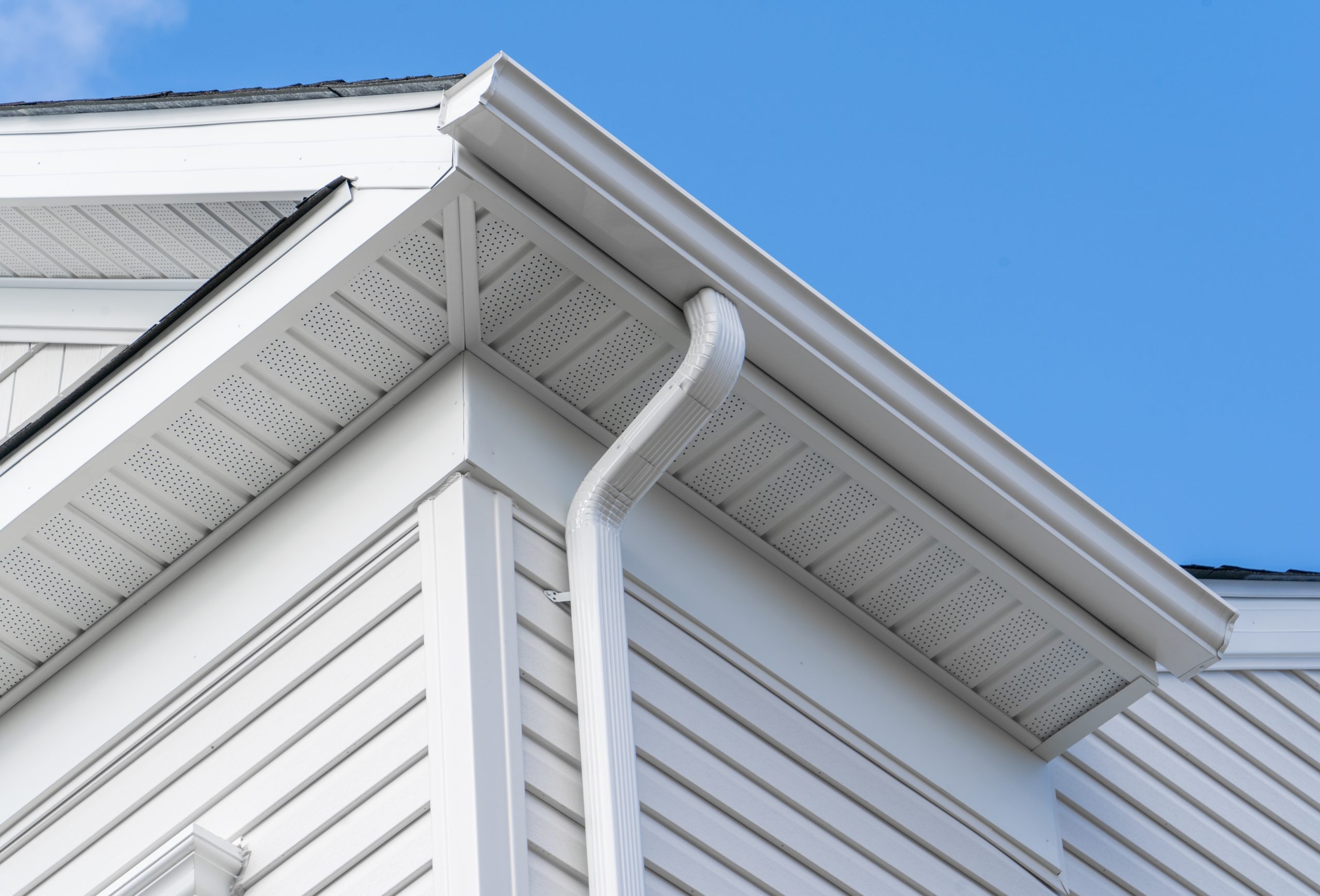 Colonial white fiber cement horizontal vinyl lap siding, soffit with ventilation, gutter and guard, eaves with elbow, drip, on a new construction American single family home